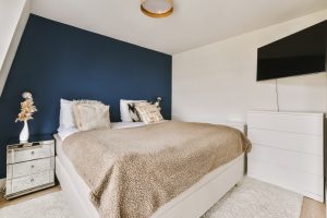 a bedroom with a bed, dressers and tv on the wall in front of the bed is dark blue