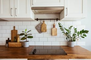 Kitchen brass utensils, chef accessories. Hanging kitchen with white tiles wall and wood tabletop.Green plant on kitchen background side view